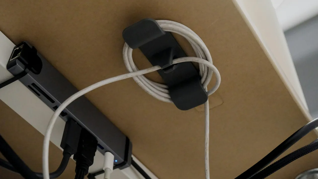 Under-desk cable organizer holding a coiled white cord next to a mounted USB hub